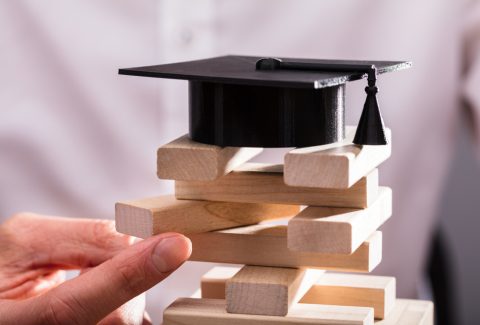 Graduation,Hat,Over,Businessperson's,Hand,Arranging,Wooden,Blocks